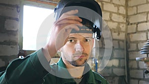 Welder opens mask and looking at camera. Portrait of handsome man with beard working in his garage or workshop. Slow