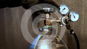 A welder in protective gloves opens a gas cylinder valve with pressure gauge