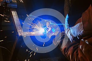 Welder in a protective mask in a dark shop floor weld metal parts. Sparks flyng