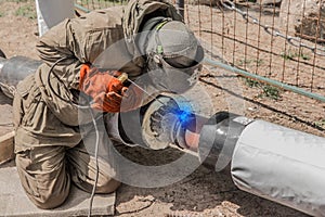 A welder in a protective shield is engaged in welding work on the polyethylene pipe of the heating main pipeline at the