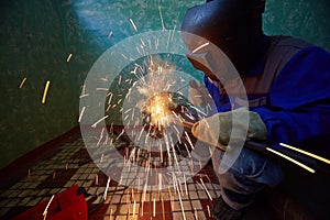 Welder in protective suit and mask welds metal pipes