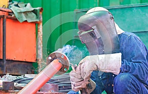 Welder with safety equipment is welding metal flange to connect with steel pipe for use improving oil pipeline systems work