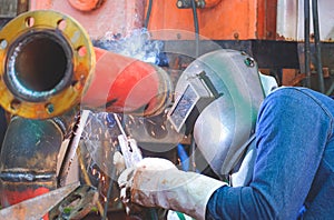 Welder with safety equipment is welding steel pipe in outdoors workshop for use in oil pipeline system renovate work