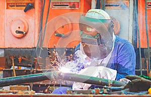 Welder with safety equipment is welding steel pipe at workshop for using in oil pipeline system renovate work