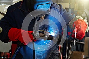 A welder wearing a protective mask and red gloves