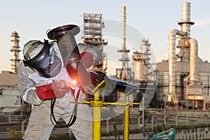 Welder is welding in factory on oil refinery plant background