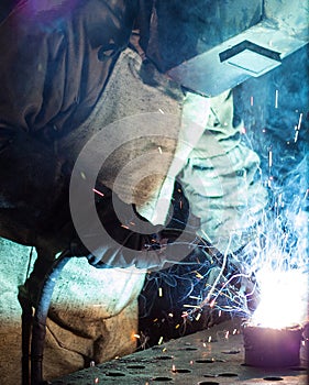 A welder in a welding mask and protective suit welds metal parts, welding and sparks, smoke, worker