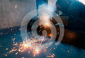 Welder welding metal with argon arc welding machine and has welding sparks. Man wears a welding mask and gloves. Safety in