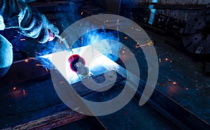 Welder welding metal with argon arc welding machine and has welding sparks. A man wears protective gloves. Safety in industrial