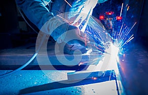 Welder welding metal with argon arc welding machine and has welding sparks. A man wears protective gloves. Safety in industrial