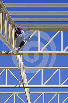 Welder is welding metal on roof structure of warehouse building in construction site against blue sky