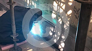 Welder is welding parts of industrial building with lots of bright sparks