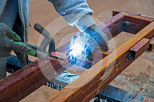 Welder welding two iron profiles at the construction site on a sunny day