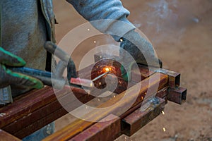 Welder welding two iron profiles at the construction site on a sunny day