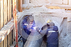 Welder welding water or gas steel pipeline with assistant worker in trench. City underground utilitites renewal and replacemen photo