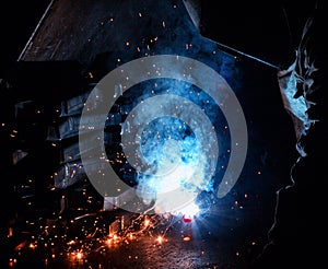 Welder welds metal parts, many sparks and fumes, welding, welding arc, bright flash, close-up, factory