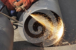 Welder worker welding a wide metal pipe tube with a oxy-fuel cutting torch, with flame and sparks