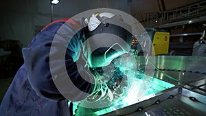Welder is working with metal details at workshop of plant, wearing mask