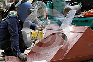 Welder working in a welding mask weld metal with arc welding machine at construction site