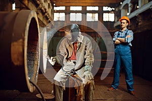 Welder works on factory, worker on background