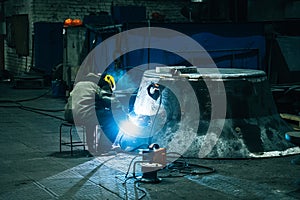 Welder works in industrial workshop. White flashes and welding smoke