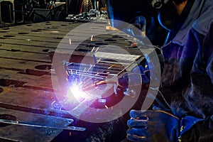 A welder in a workshop joins parts with a weld, sparks and smoke from welding