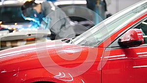 Welding industrial: worker in helmet repair detail in auto service in front of the red car