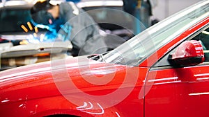 Welding industrial: worker in helmet repair detail in auto service in front of the red car