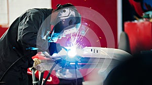 Welding industrial: worker in helmet repair detail in car auto service - blue sparklers