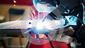 Welding industrial: worker in helmet repair detail in car service