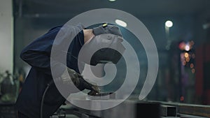 welding work at a metalworking plant. A helmet welder welds a metal part on a welding table. Welding of steel, sparking