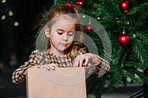 Well behaved girl sitting under a christmas tree, looking at wrapped present