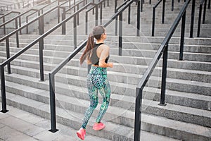 Well-built and shaped young woman jogging. He runs up on stairs. Girl wear good sports uniform. Her hair braids in