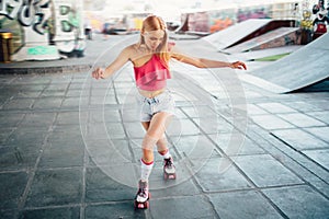 Well-built and slim girl is posing on camera. She is looking down to her knees and rollerblading. She is doing that very