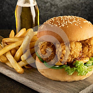 a well crafted southern fried chicken burger served with a side of fries and a bottle of beer