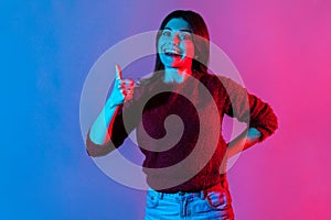 Well done, good job! Neon light portrait of joyful brunette woman showing thumbs up, like gesture to camera