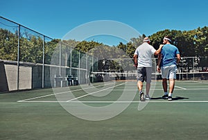 Well done today. Full length shot of two unrecognizable sportsmen walking together on a tennis court after a training
