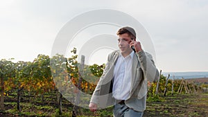 Well-dressed businessman talking on the phone while walking on the edge of his vineyard. Commercial video.