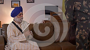 Well-dressed soldier following Indian rituals of touching his father`s feet - a Sikh family of India