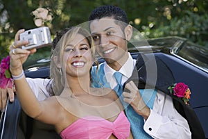 Well-dressed teenage couple taking picture outside car