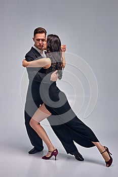 Well-dressed young couple dancing tango over grey studio background