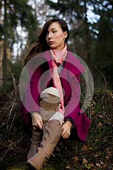 Well-dressed young woman in pink topcoat sitting in forest