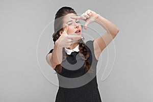 Well dressed young woman showing frame sign and wink