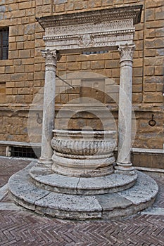 Well in front of a church wall at small square in Pienza , Siena province, Tuscany