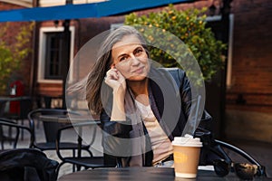 Well-groomed gray-haired woman of 60 years old at  cafe table with coffee
