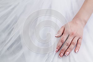 Well-groomed hand of the bride with a beautiful manicure on a white wedding dress