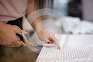 Well groomed woman hands cutting polka dot fabric with tailor scissors for sewing dress in studio