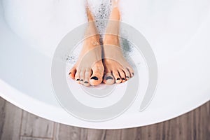 Well groomed woman`s legs in bath foam close up image