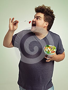 Well hello little tomato. Studio shot of an overweight man holding a bowl of salad.