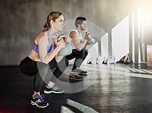 Well its not going to lift itself. two young people working out in the gym using kettle bells.